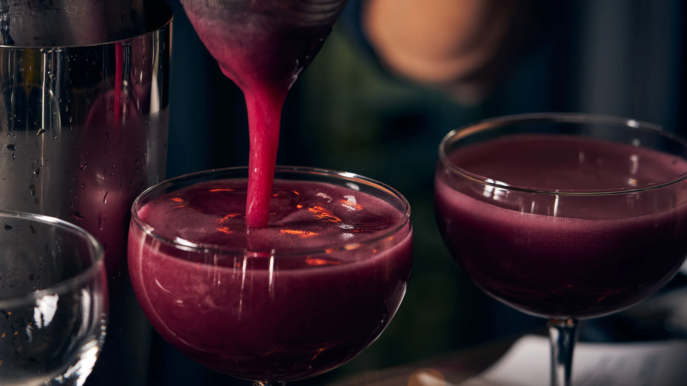 A purple cocktail being poured behind the bar